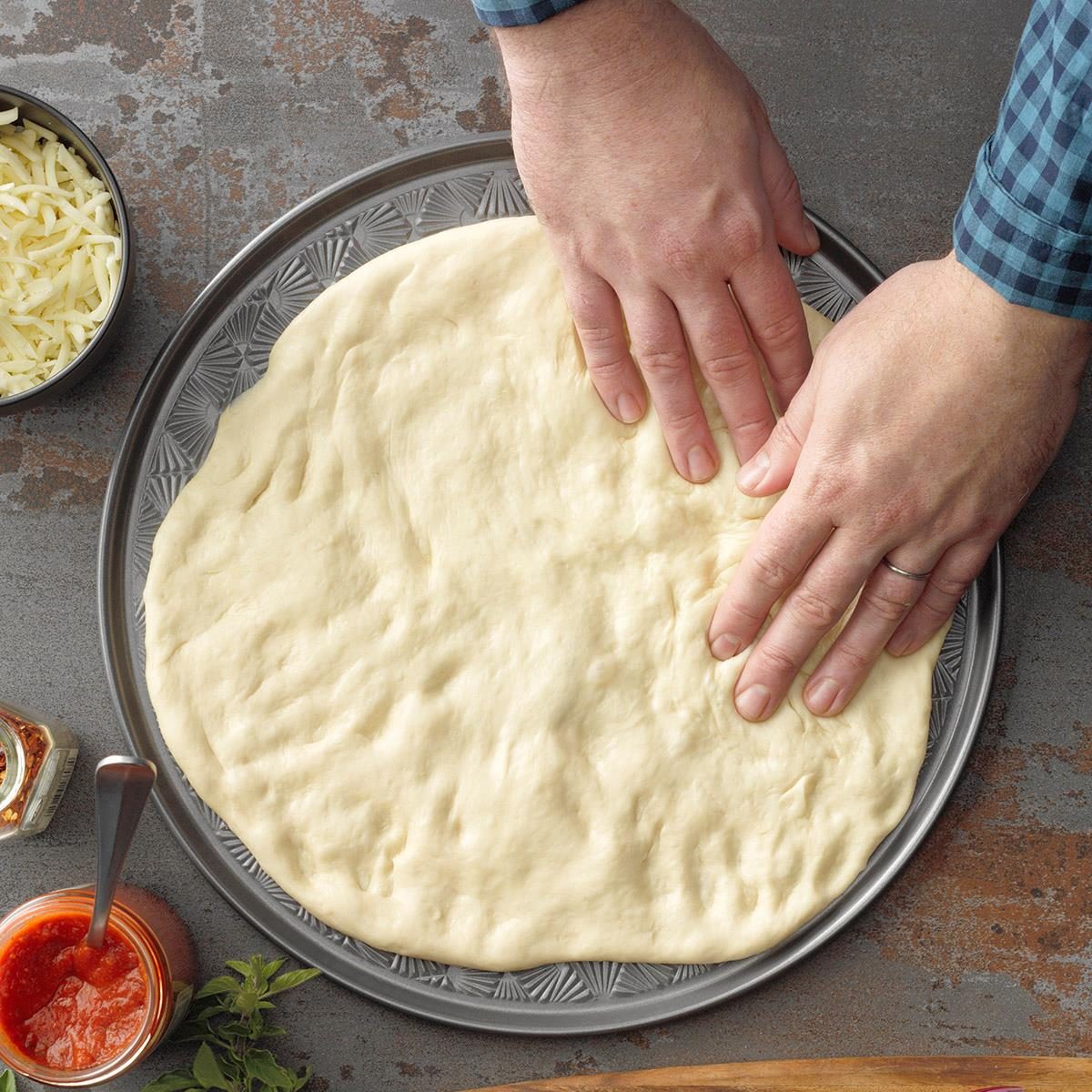hands stretching pizza dough onto a baking pan
