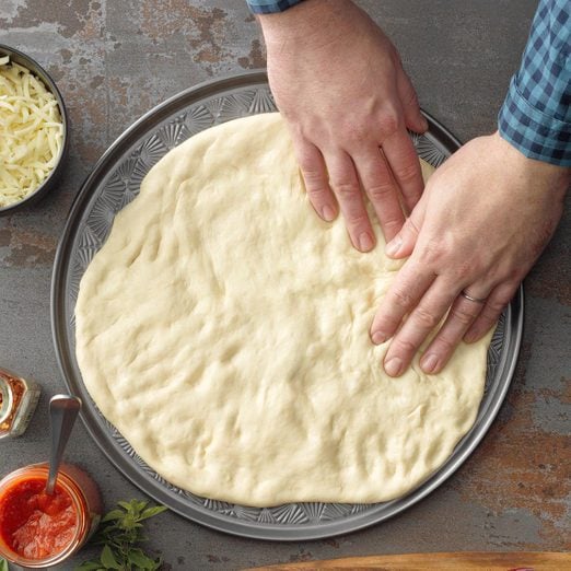 hands stretching pizza dough onto a baking pan