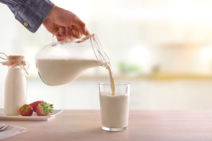 Serving breakfast milk with a jug in a glass on a white wooden kitchen table