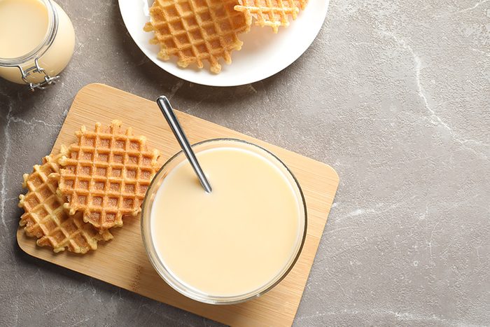 Bowl of condensed milk and waffles served on grey table