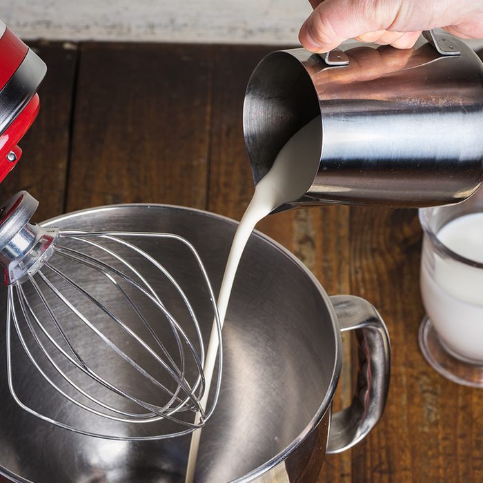 Open standing mixer with whisk on wooden table with ingredients