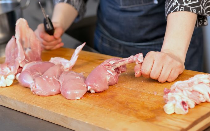 Close-up raw chicken lies in portions on the board in the kitchen of the restaurant. Professional in black uniform chef holding a knife. Master class on cutting, cooking chicken and soup