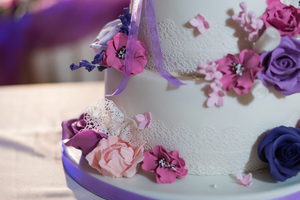 Beautiful fondant covered cake decorated with edible lace and bouquet of purple flowers