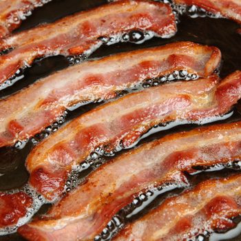 Bacon strips or rashers being cooked in frying pan.; Shutterstock ID 153808931