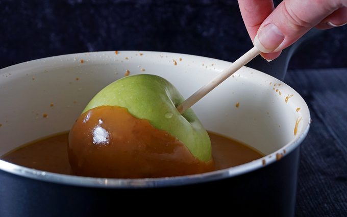 dipping a green apple into homemade caramel