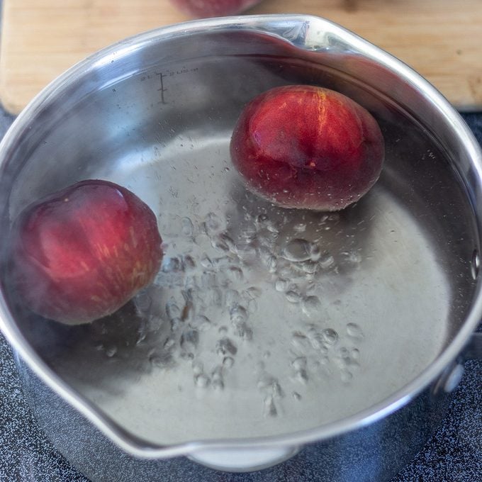 Silver saucepan with whole peaches in boiling water