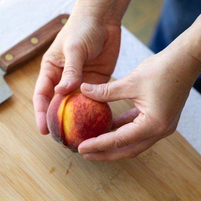 Hands holding a whole peach that is cut in half.
