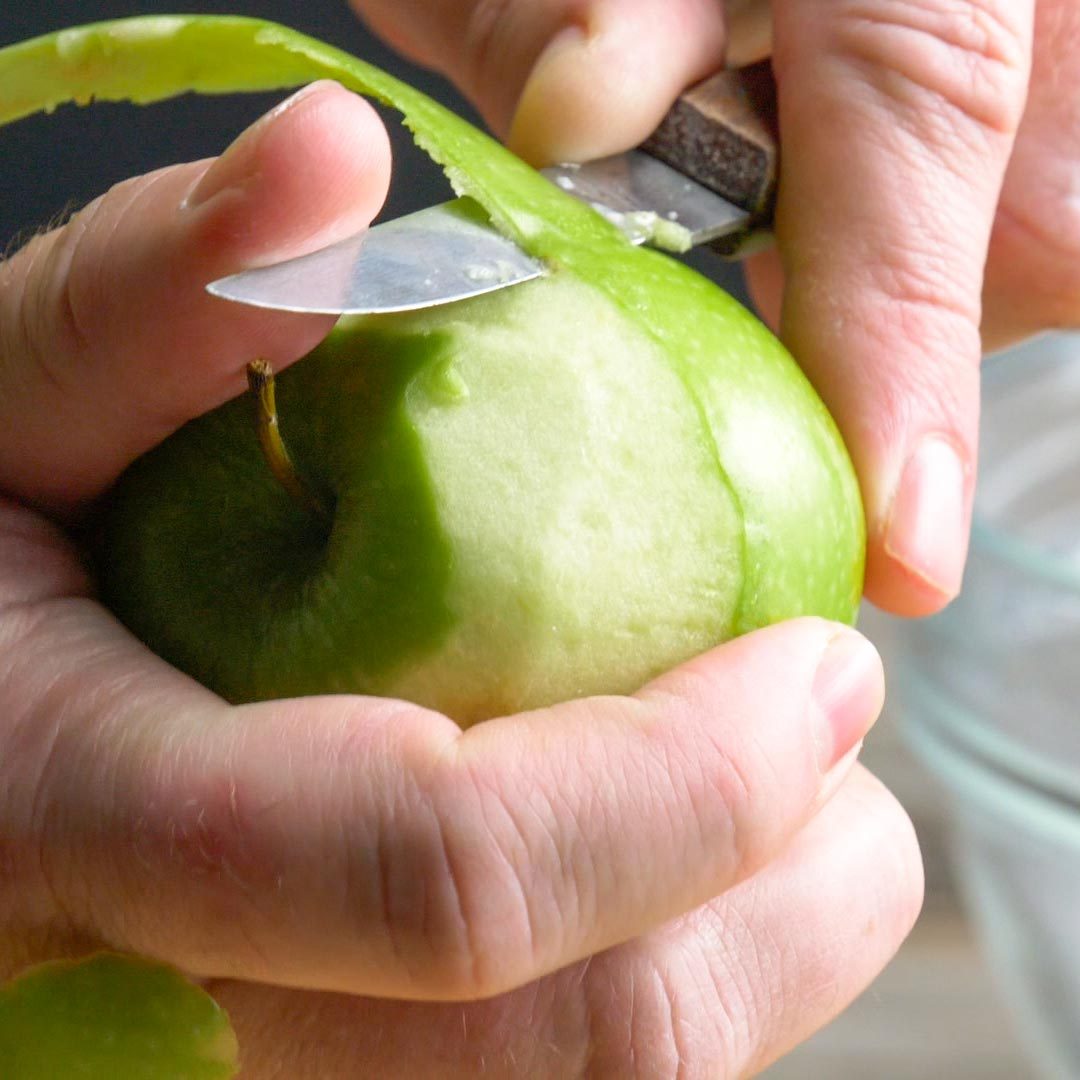 close up of hands peeling an apple with a knife for apple pie filling