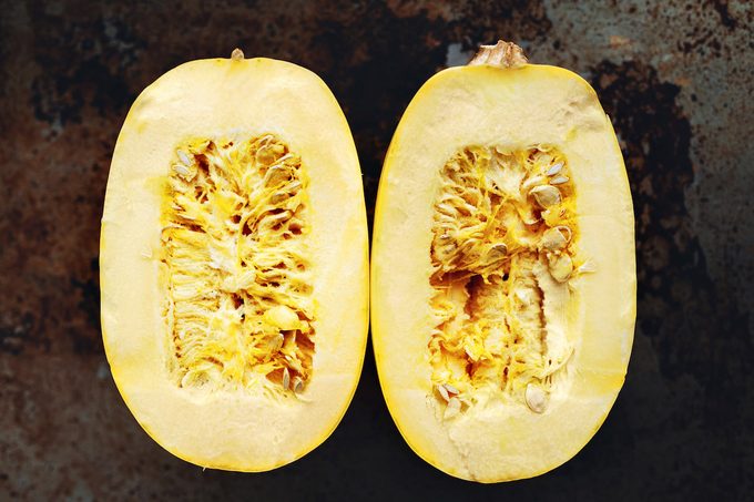 A halved raw spaghetti squash on a well seasoned baking sheet.