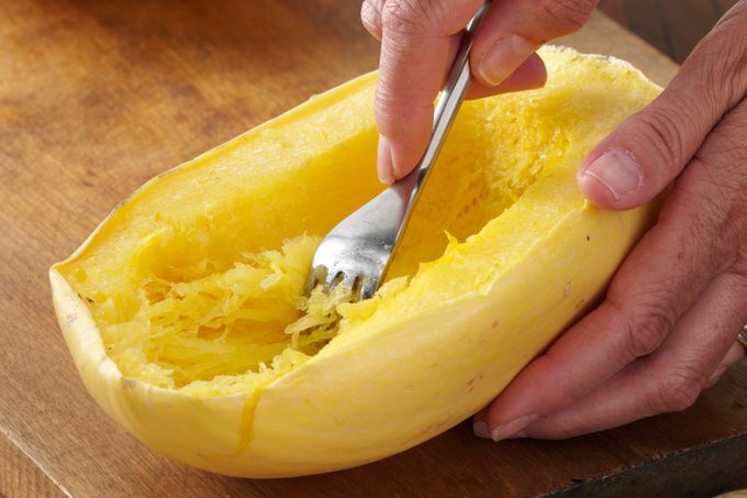A close up of someone scooping the flesh out of cooked spaghetti squash.