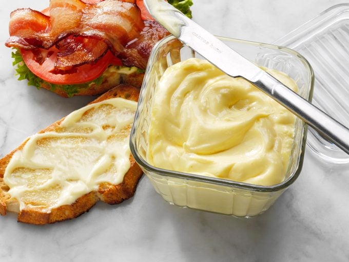 Homemade Mayonnaise in a bowl with a slice of bread with an open face BLT sandwich in the background