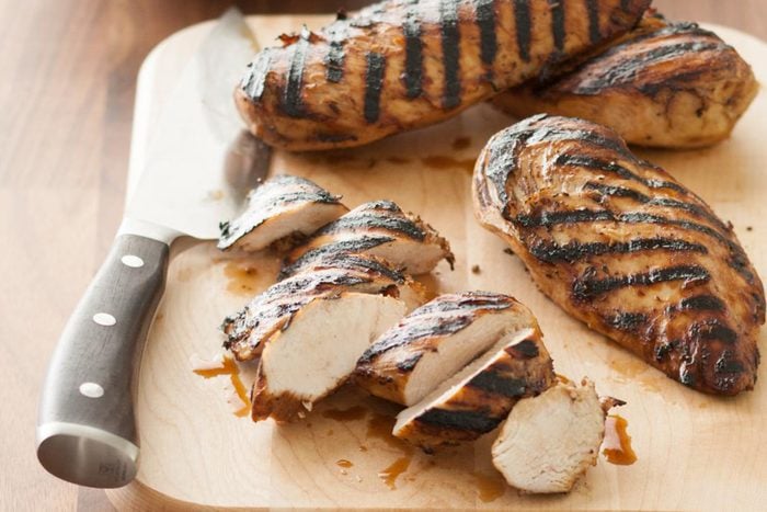 sliced and whole grilled chicken and knife on wood cutting board