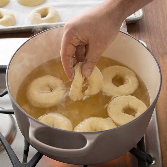 A person placing rings of dough into a boiling pot of water to make homemade bagels.