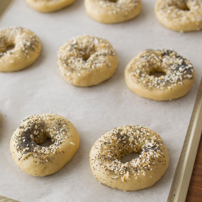 Homemade bagels arranged on a parchment-lined baking sheet.