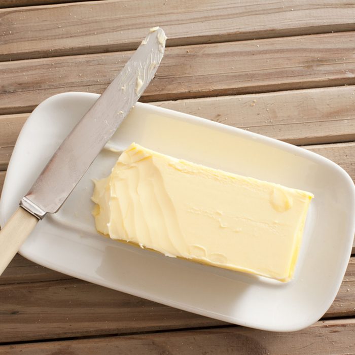 Pat of fresh farm butter on a butter dish with a knife to use as a spread or cooing ingredient, overhead view on a slatted wooden table; Shutterstock ID 327704603