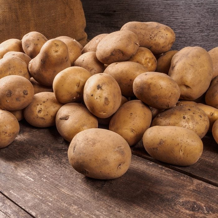 Pile of potatoes lying on wooden boards with a potato bag in the background ; Shutterstock ID 347630291