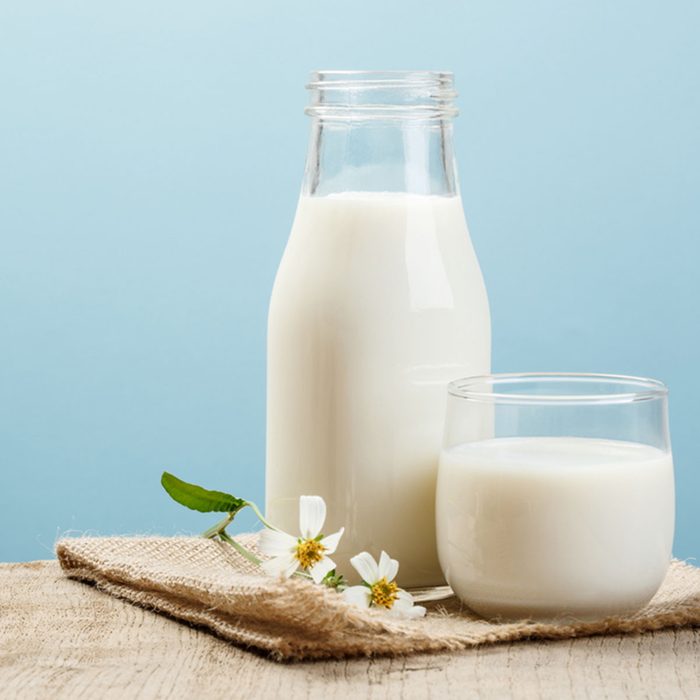 A bottle of milk and glass of milk on a wooden table on a blue background; Shutterstock ID 568076731