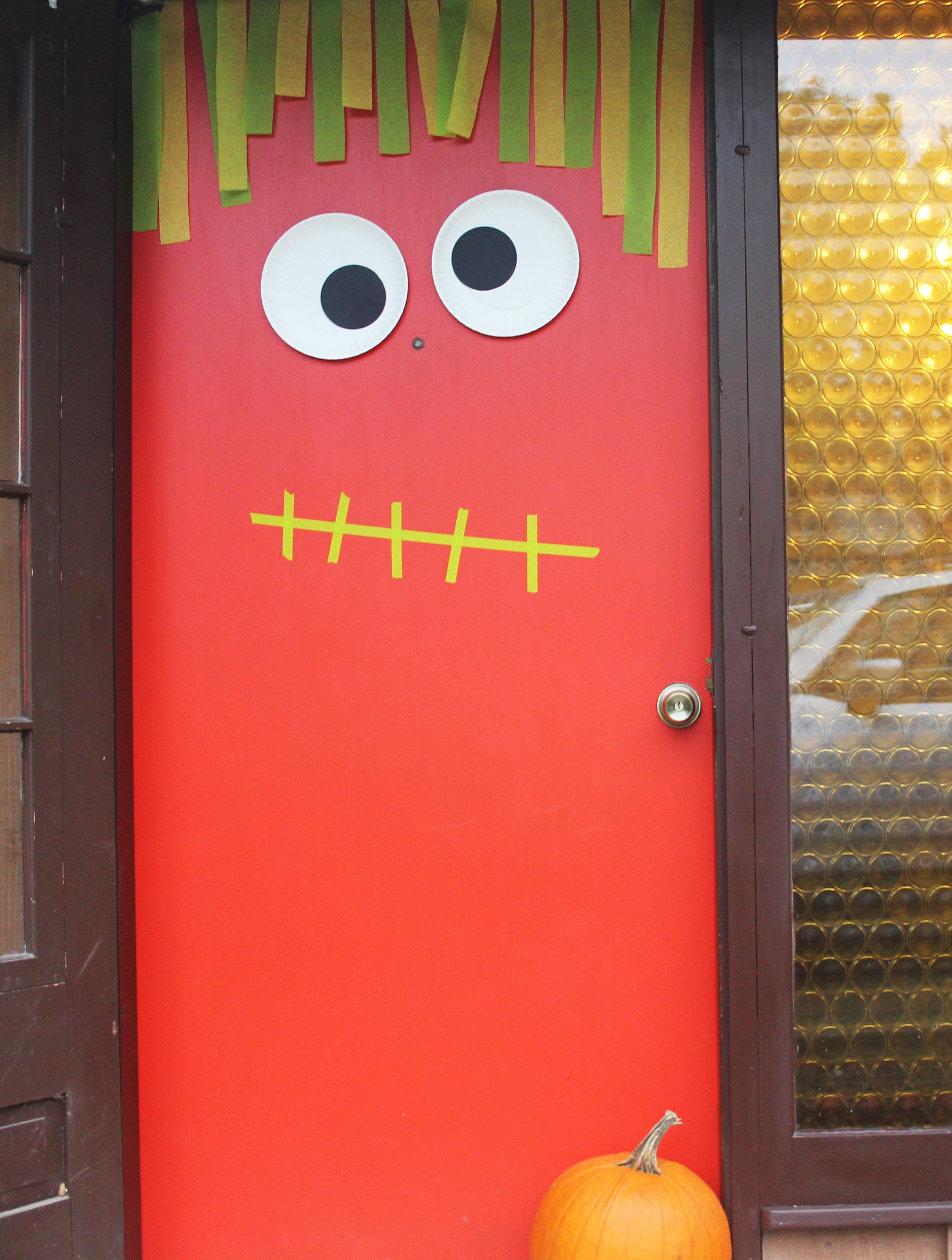 Bright red door with cut-out eyes and stripe of paper hanging down like hair