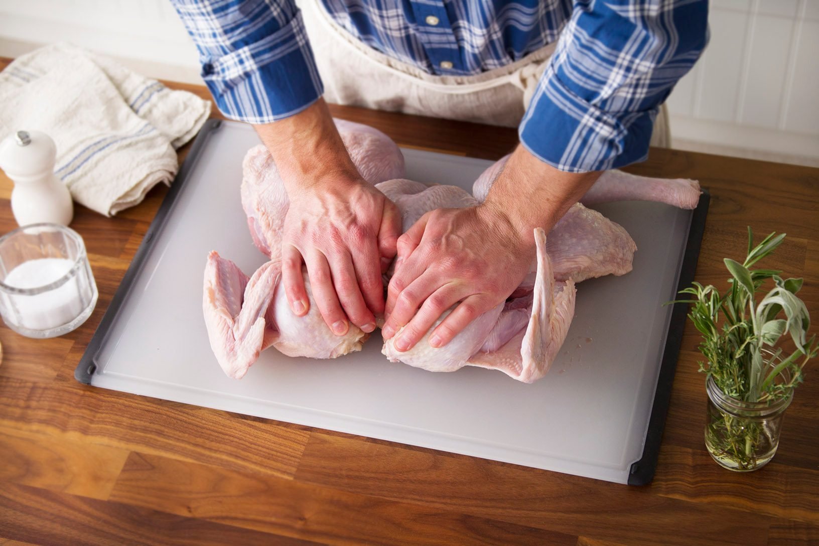 Person pressing a raw turkey down flat on a cutting board with one hand on each side of its breast