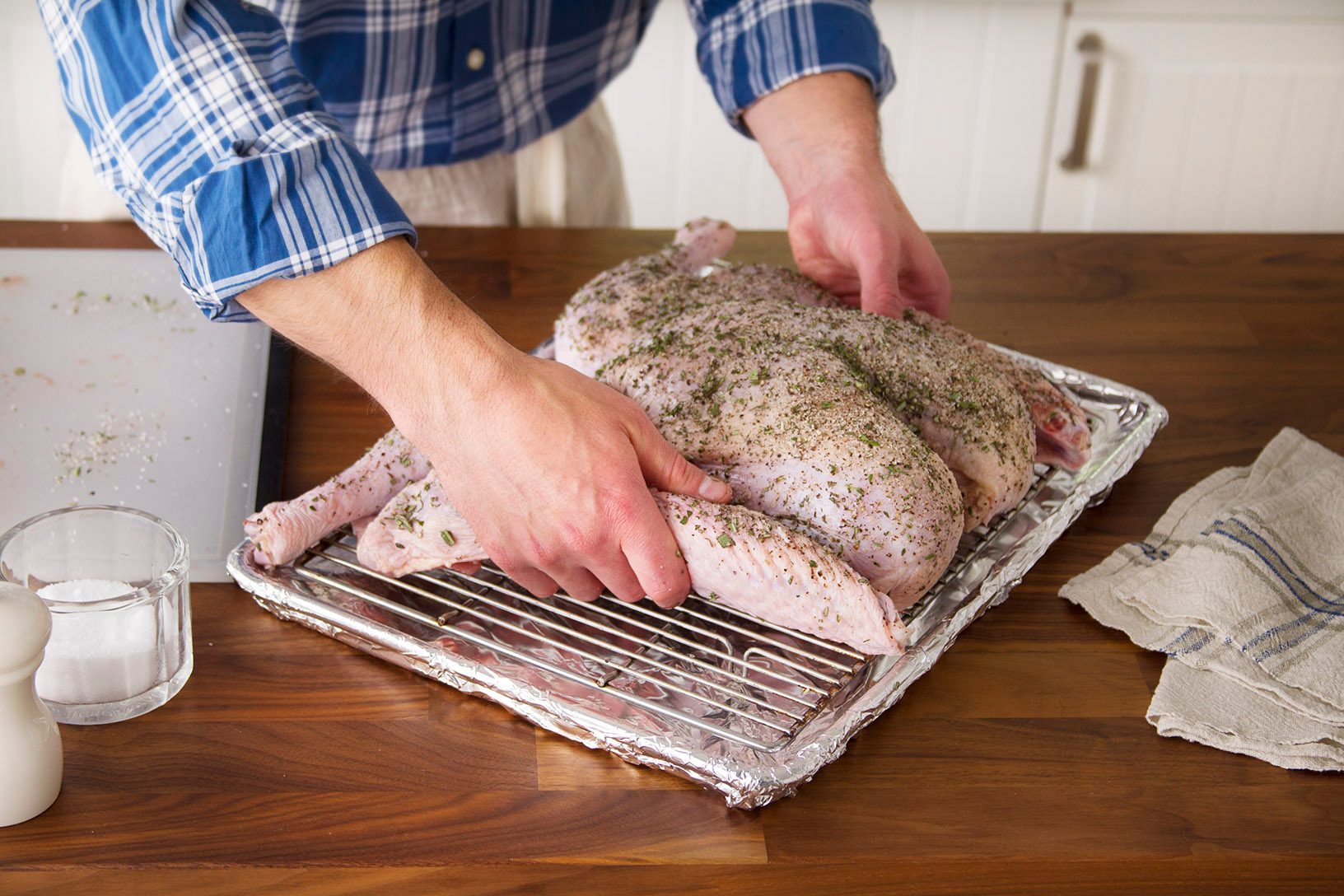 Person setting down a raw turkey down on a sheet pan with a rack inside it