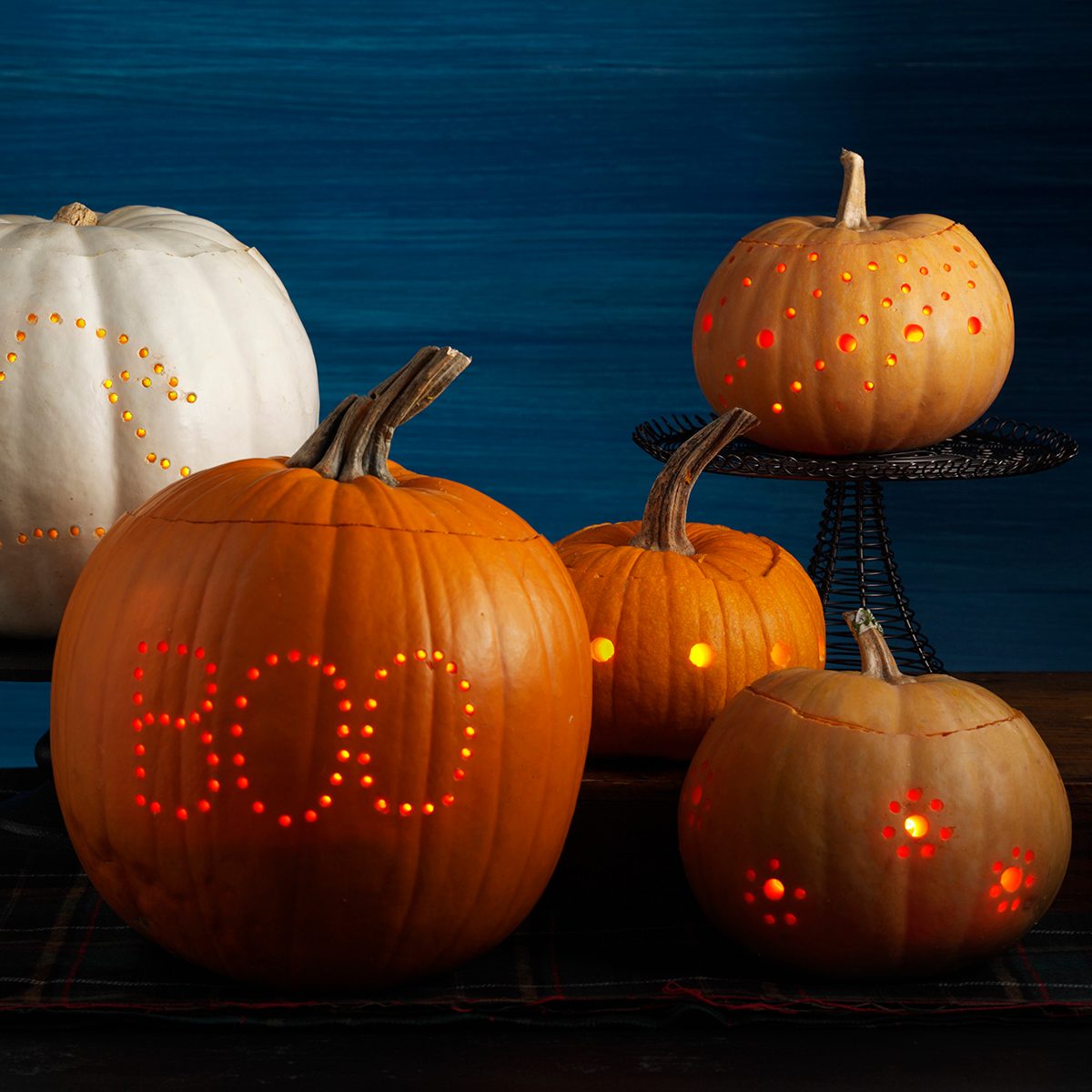 Five illuminated jack-o-laterns that are carved with mini holes that form different patterns and designs