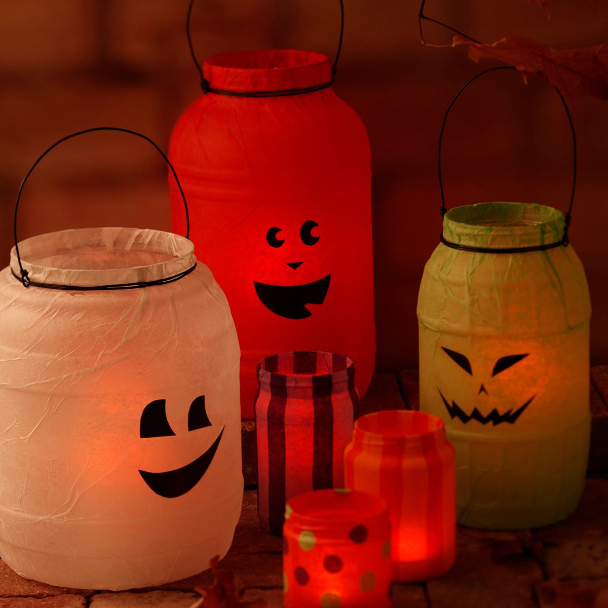 Mason jars covered in halloween-themed tissue paper like ghosts, jack-o-lantern and monsters lit up by candles