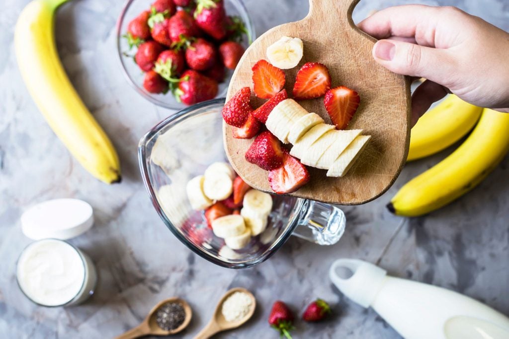 Ingredients for making strawberry banana smoothies next to a blender