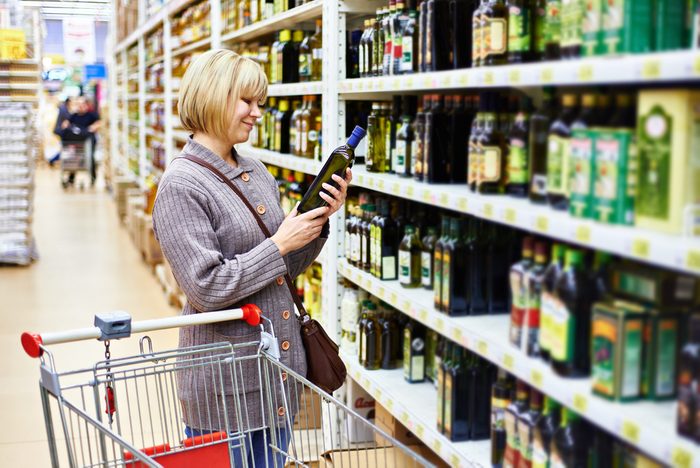 Woman reading the label on a bottle of olive oil in the store; Shutterstock ID 245223466; Job (TFH, TOH, RD, BNB, CWM, CM): TOH Cooking Oils