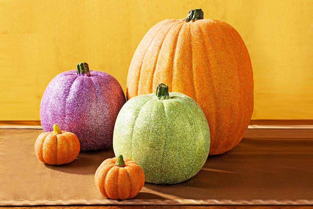 different colored glitter pumpkins on a wood surface with a yellow background
