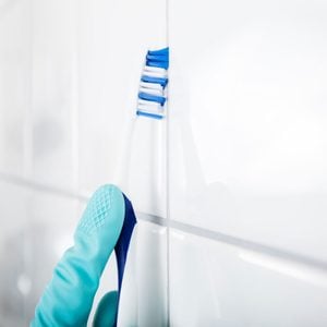 Close-up Of Person Hand Cleaning The Dirty White Tile Of The Wall Using Brush