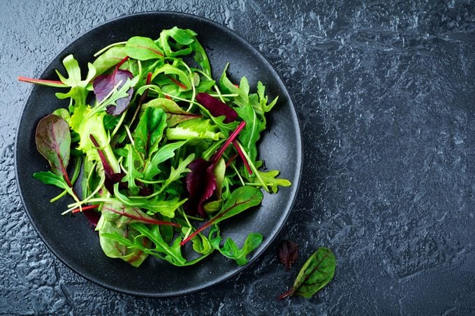 Mix fresh leaves of arugula, lettuce, spinach, beets for salad on a dark stone background.