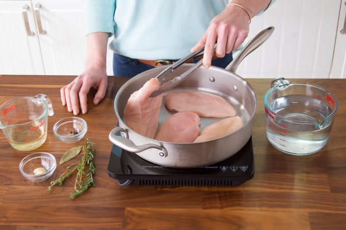 Person placing raw chicken into a pan on the stovetop with metal tongs