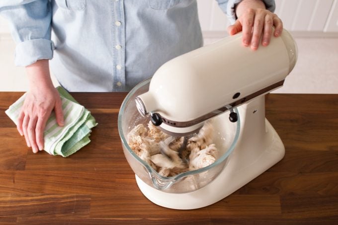 Chicken being shredded in a mixer on a wooden countertop