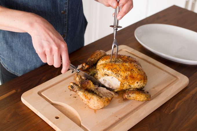 With one hand holding a fork to keep the chicken steady, a leg is sliced cleanly through on a wooden cutting board