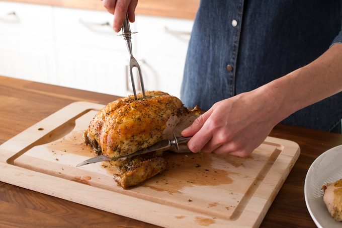 Person using a fork to steady a cooked chicken as they slice into the middle of the breast