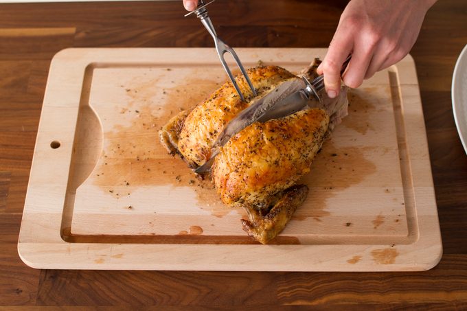 Person slicing into the top of the chicken breast on a wooden cutting board