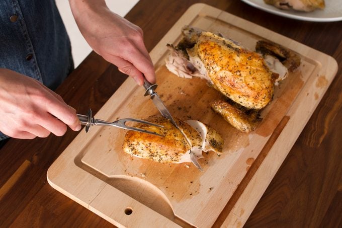 Person slicing into the chicken breast pieces on a wooden cutting board