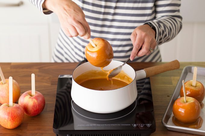 Person pulling a homemade caramel apple out of a pot of melted caramel