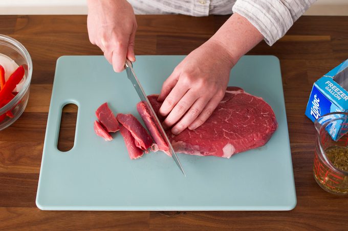 Person using a knife to slice raw beef on a cutting board