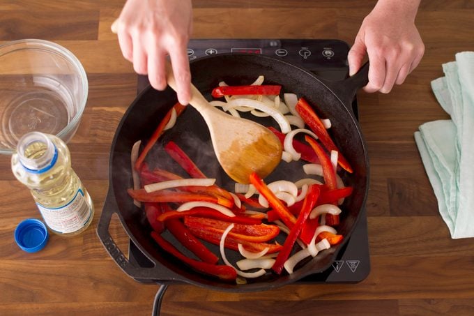 Sliced veggies in a cast-iron skillet being stirred by a wooden spoon