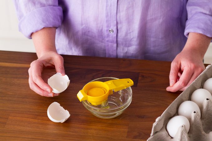 Egg separator over a small glass with a carton of eggs on the side