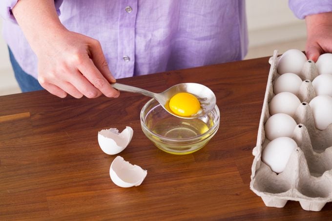 Person holding the insides of an egg inside a slotted spoon to separate out the whites