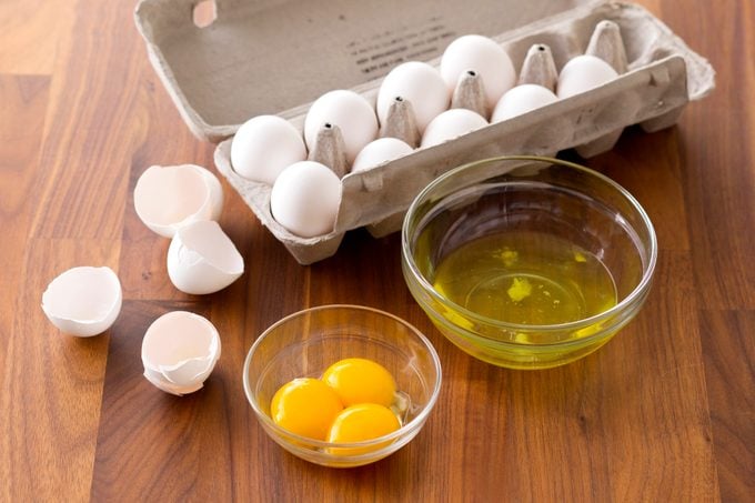 Carton of eggs besides two bowls one with egg whites and the other with yolks