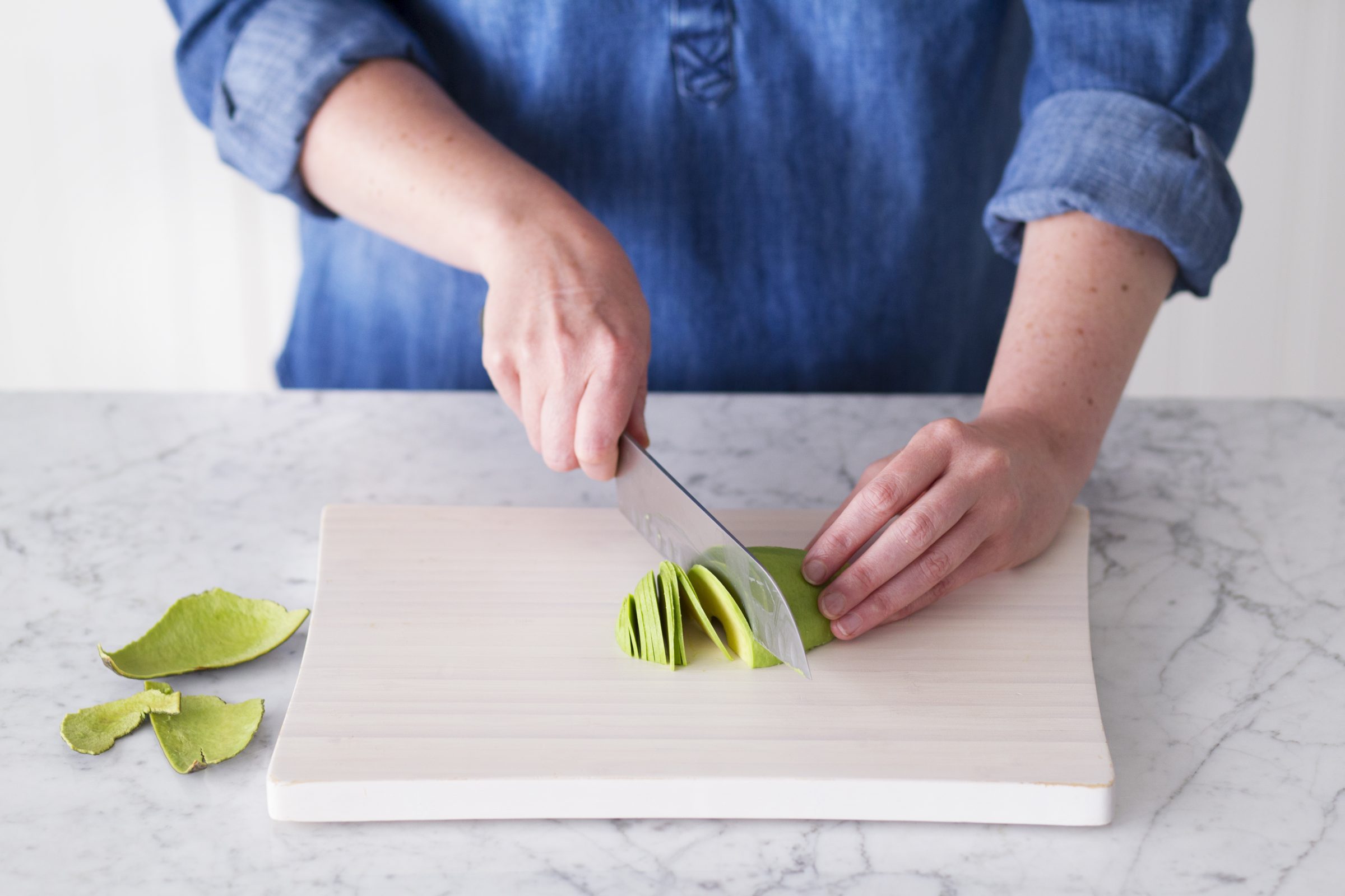Person using a knife to slice a peeled avocado half