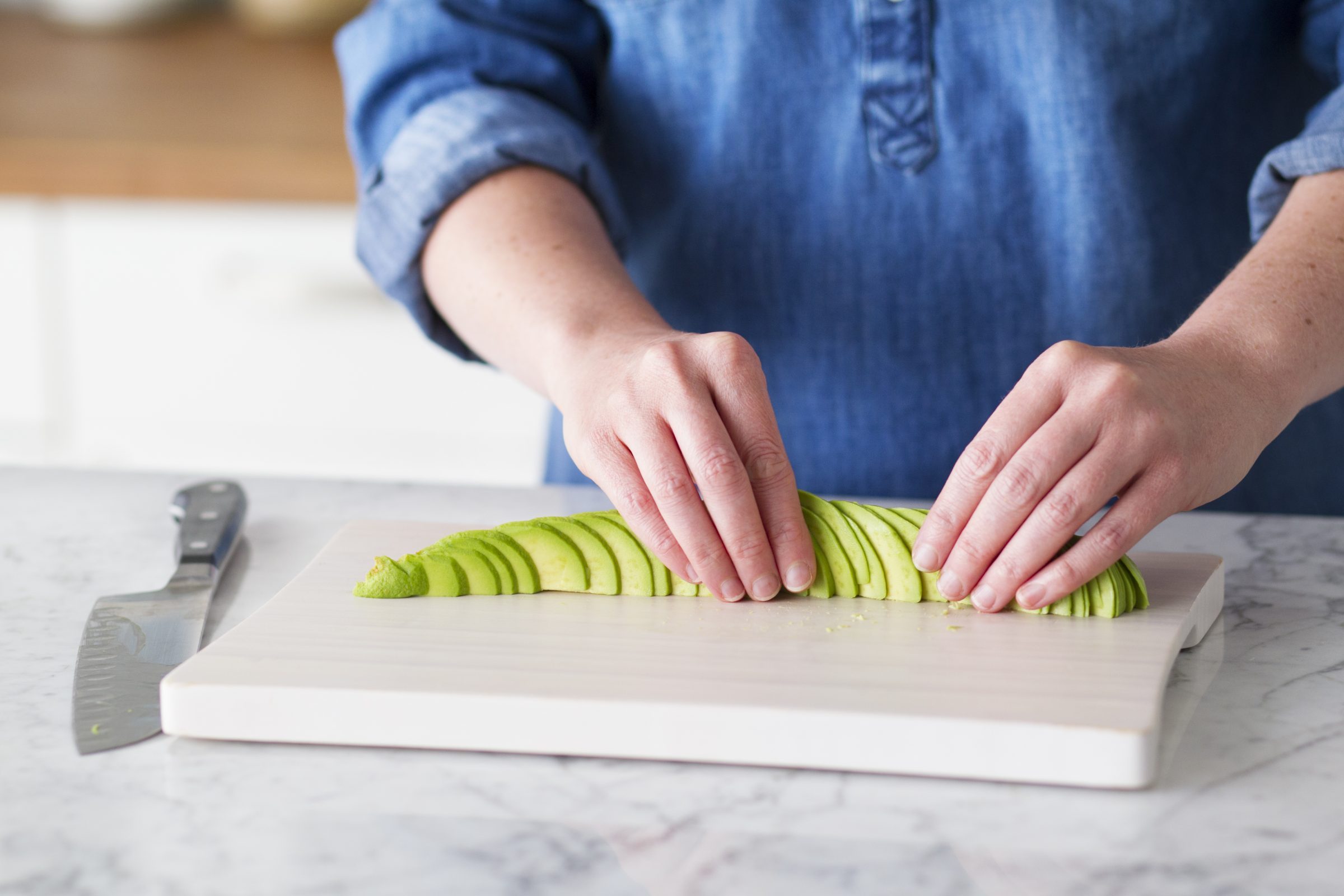 Person fanning out the slices of avocado in a line on their cutting board to make an avocado rose