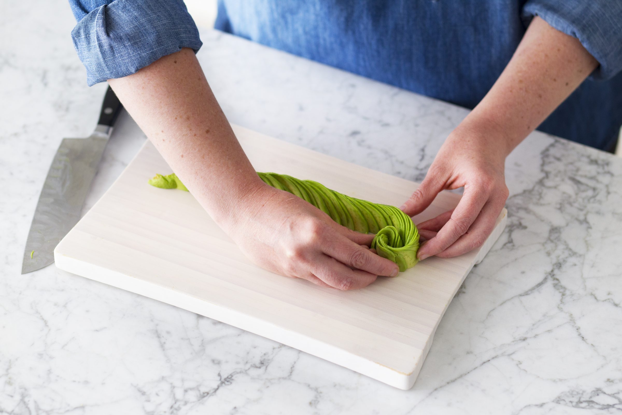 Person carefully twisting the fanned slices of avocado together into an avocado rose