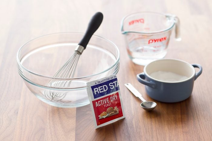Packet of yeast, measuring cups and a small spoon beside a glass bowl with a whisk in it