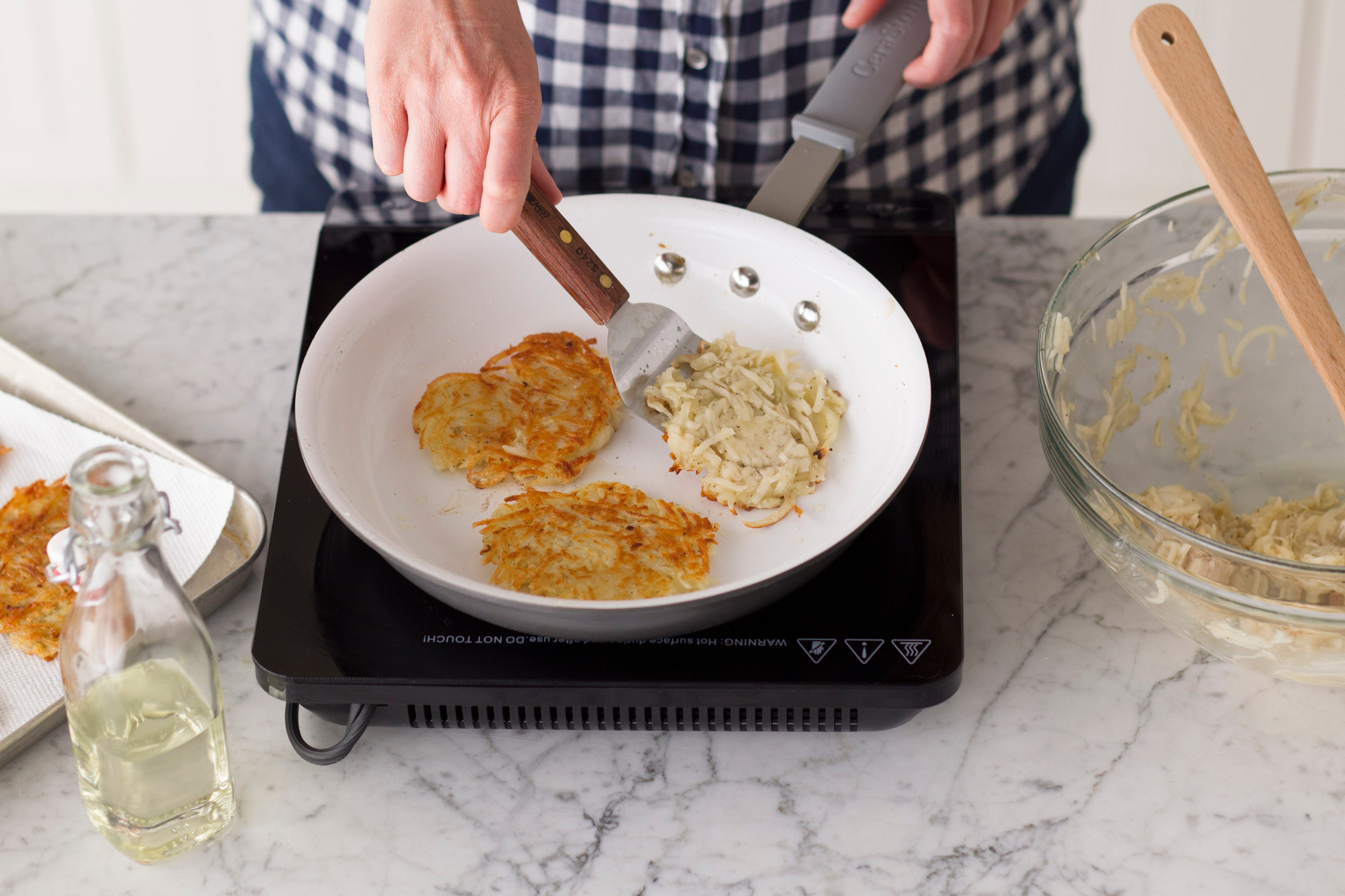 Metal spatula flipping potato pancakes as they fry in a skillet