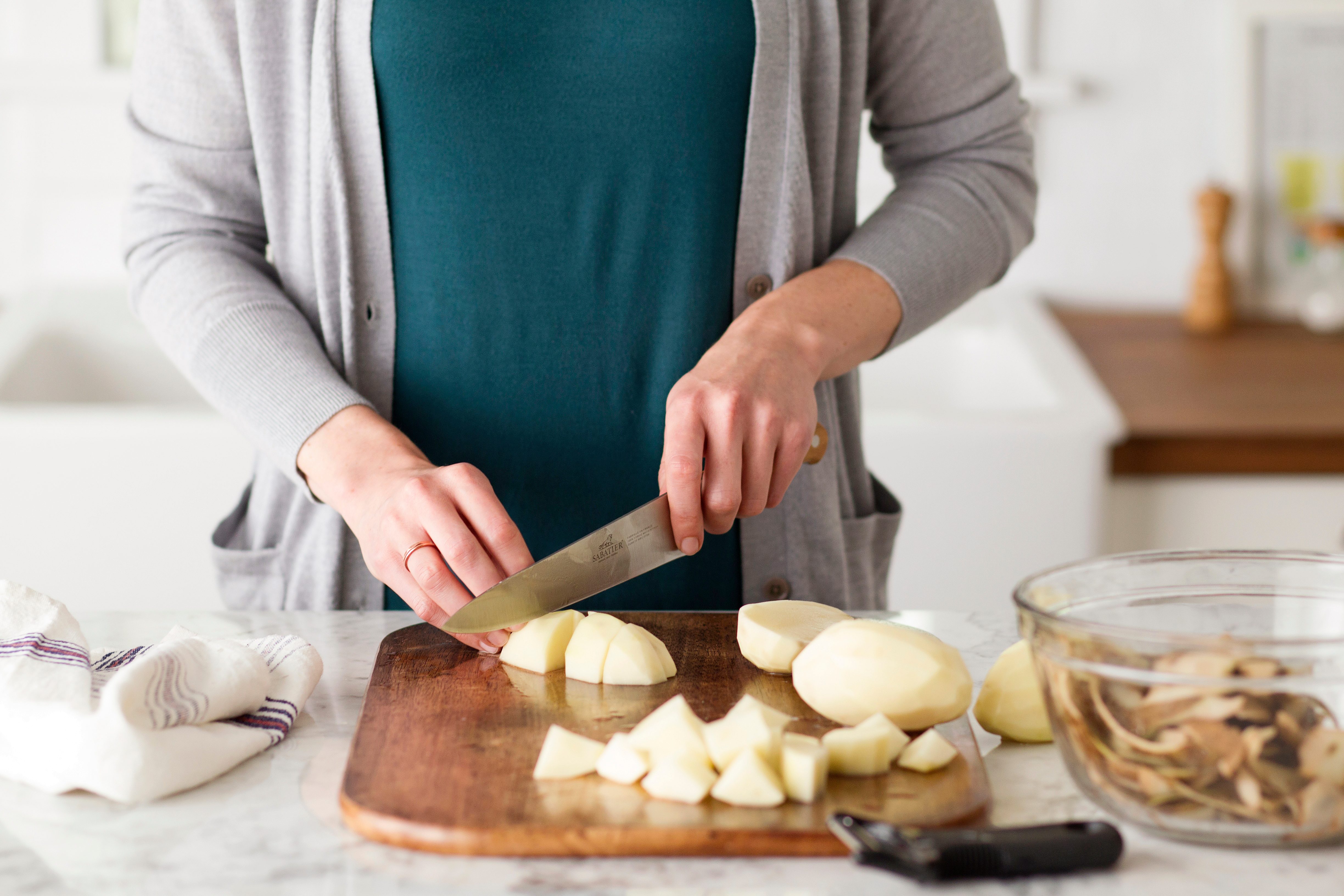 Person using a knife to chop peeled potatoes into cubes