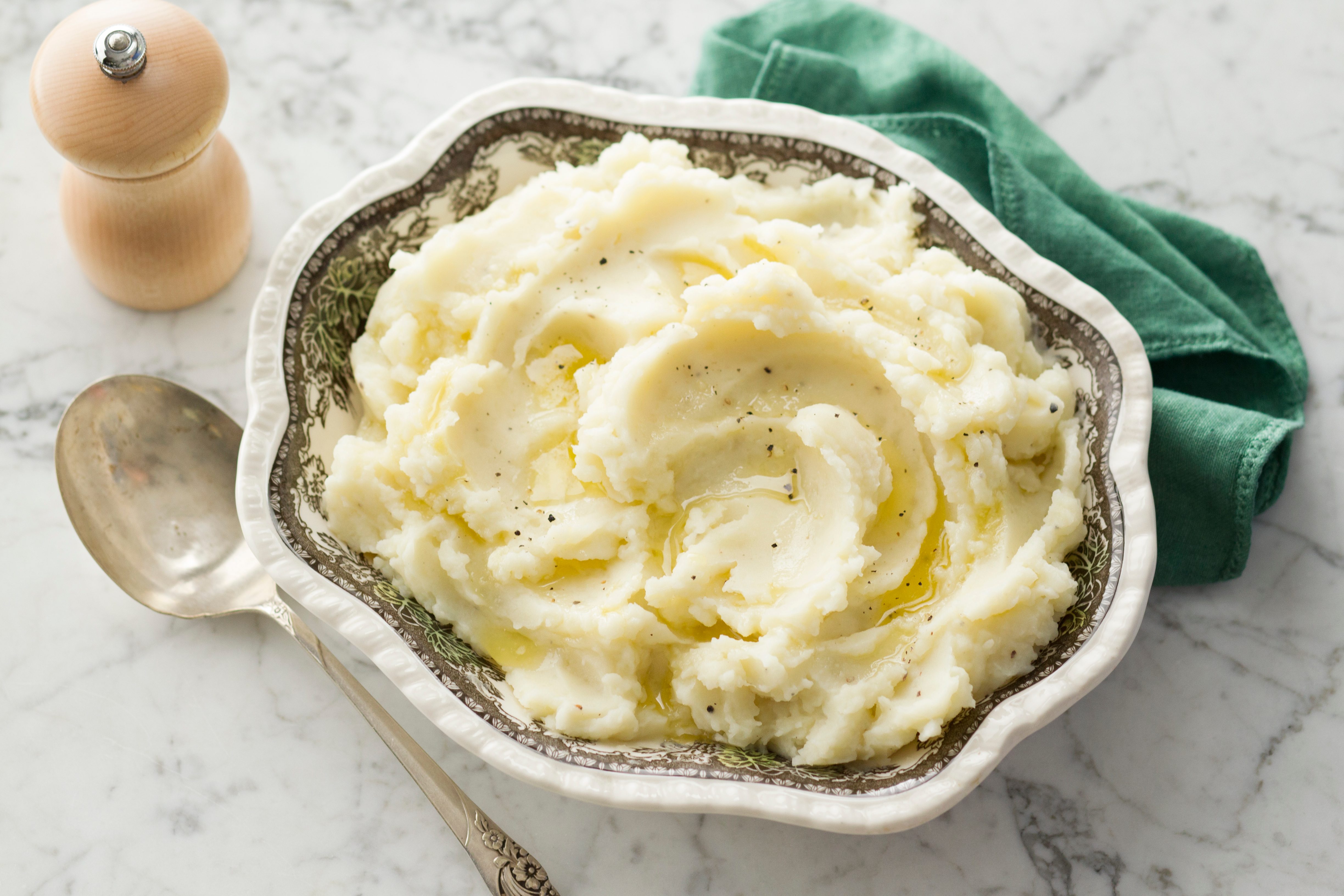 mashed potatoes in a serving dish with a kitchen towel serving spoon and pepper ginger in the background